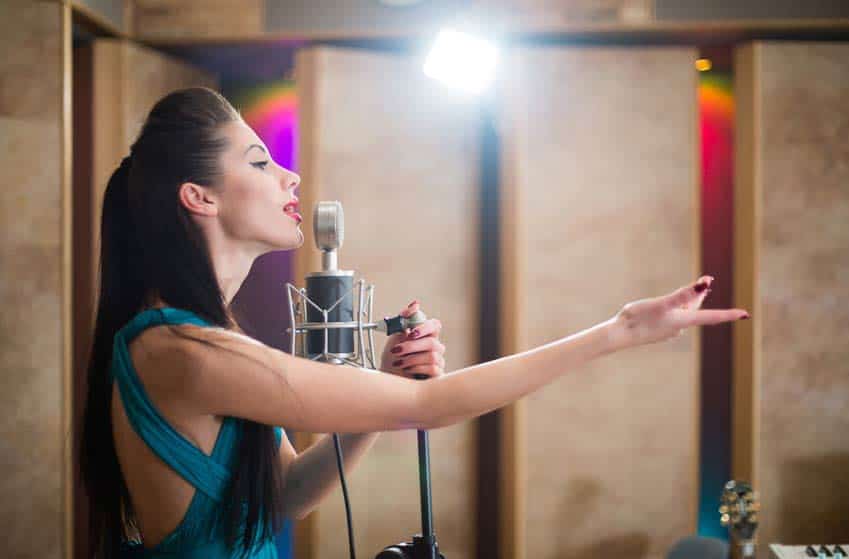 Young woman singing into microphone in recording studio