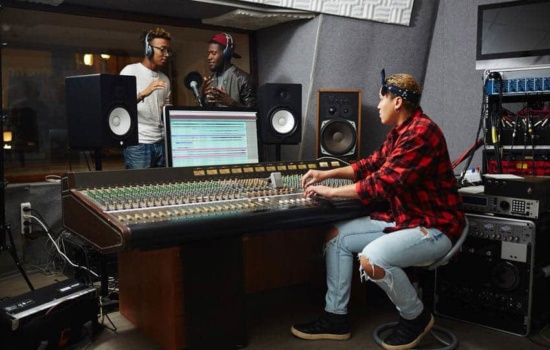 Female audio engineer using autotune software on two male vocalists in recording studio