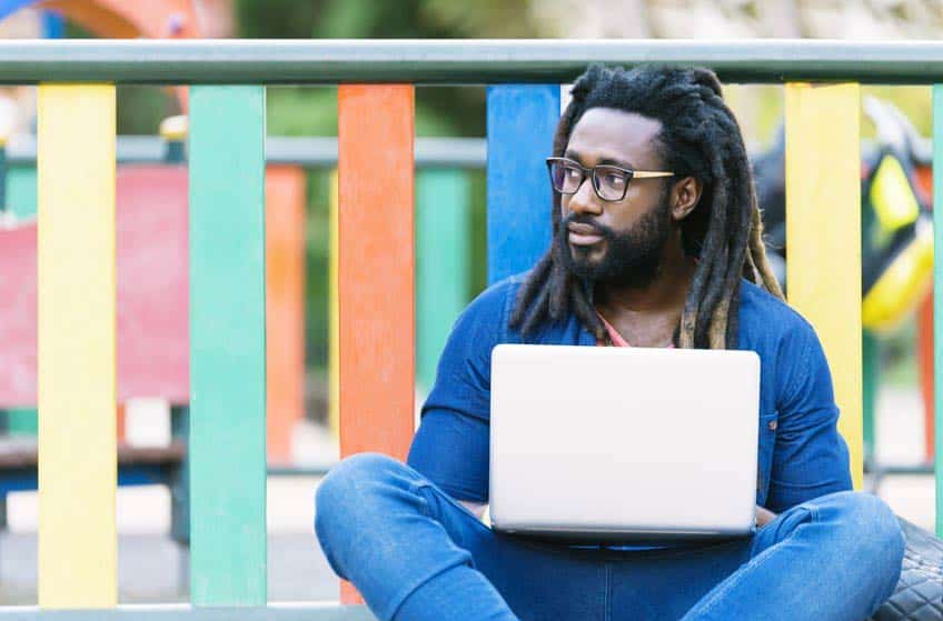 Young man with dreadlocks sitting outside on his laptop writing artist bio example