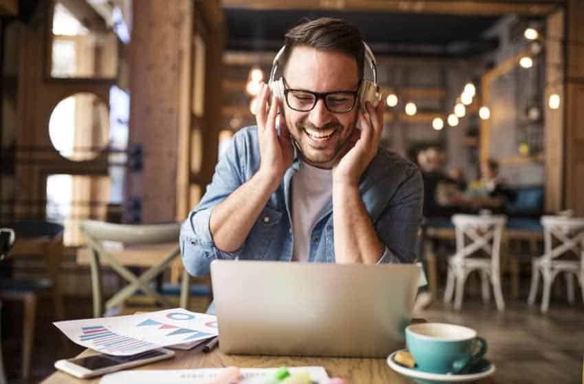 Young man with laptop and headphones listening to music in a cafe