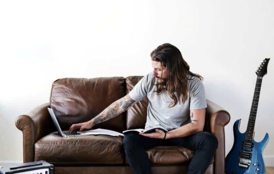 Male musician comparing music contracts to what he's seeing on his laptop