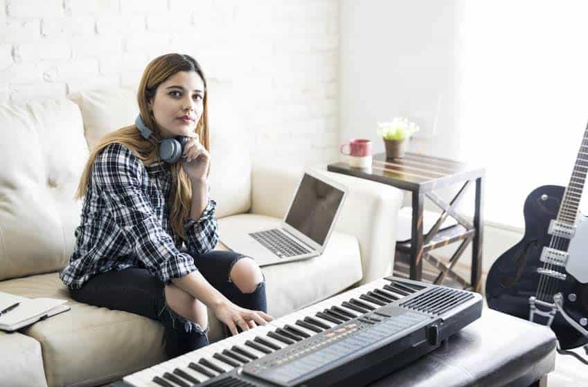 Female musician setting up mobile recording studio in her home with keyboard, guitar, and laptop
