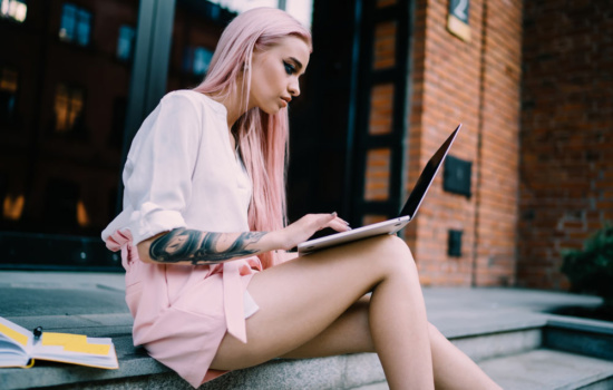 Pink-haired female musician using her laptop outdoors for music promotion