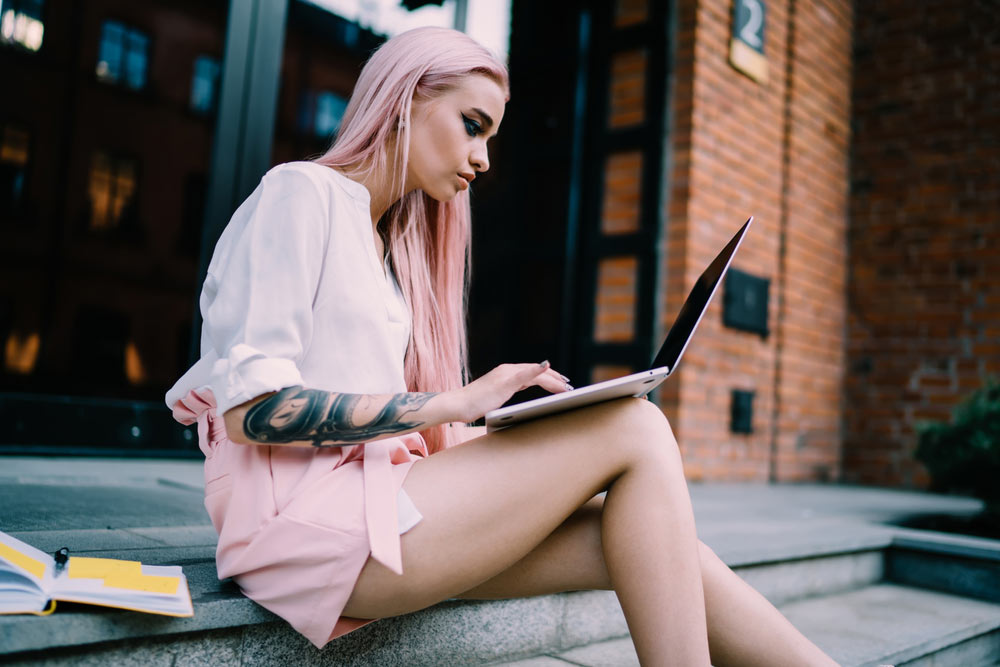 Pink-haired female musician using her laptop outdoors for music promotion