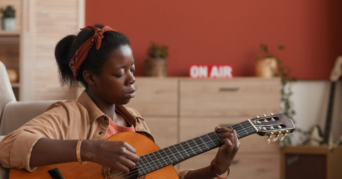 Young Black woman writing a song on her guitar