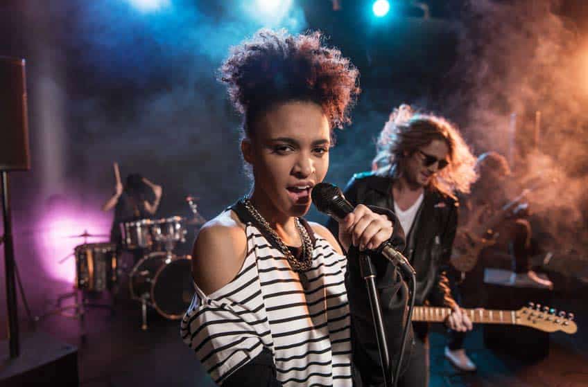 Black female rock singer onstage with white male guitarist in background