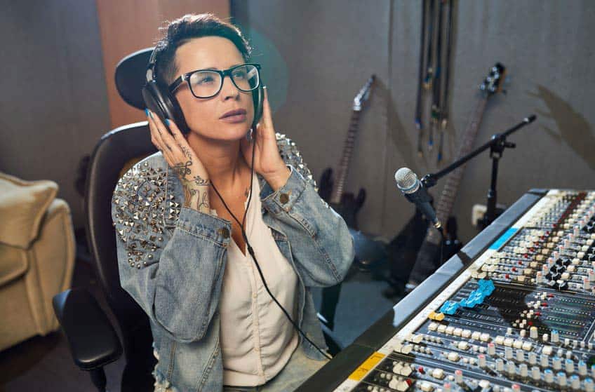Female audio engineer listening to headphones in home music studio