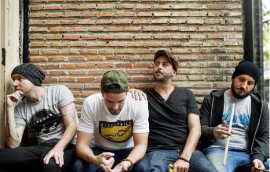 Four male bandmates sitting against brick wall