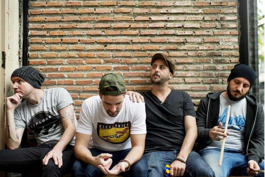 Four male bandmates sitting against brick wall