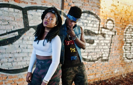 Male and female rappers standing next to graffiti-tagged wall
