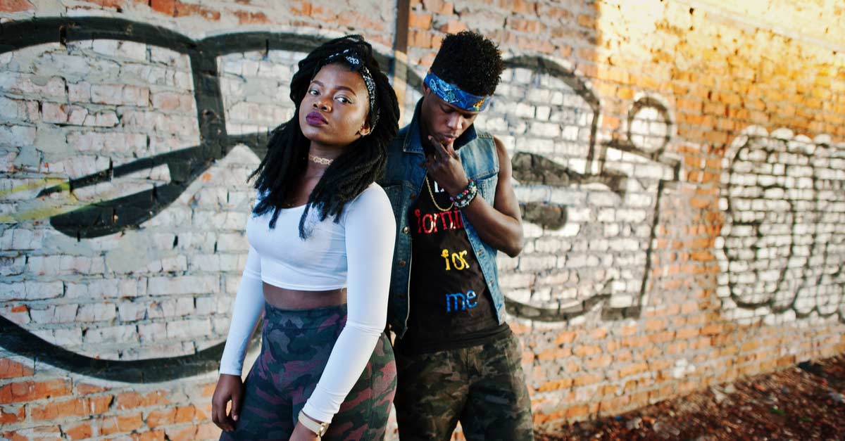 Male and female rappers standing next to graffiti-tagged wall