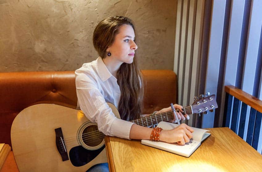 Young woman with guitar writing song lyrics