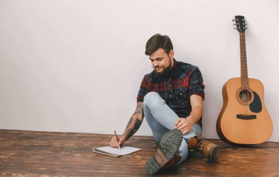 Musician songwriting with notepad and guitar