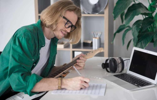 Male musician with laptop, sheet music, and guitar