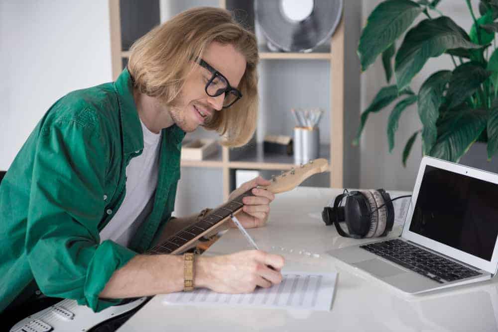 Male musician with laptop, sheet music, and guitar