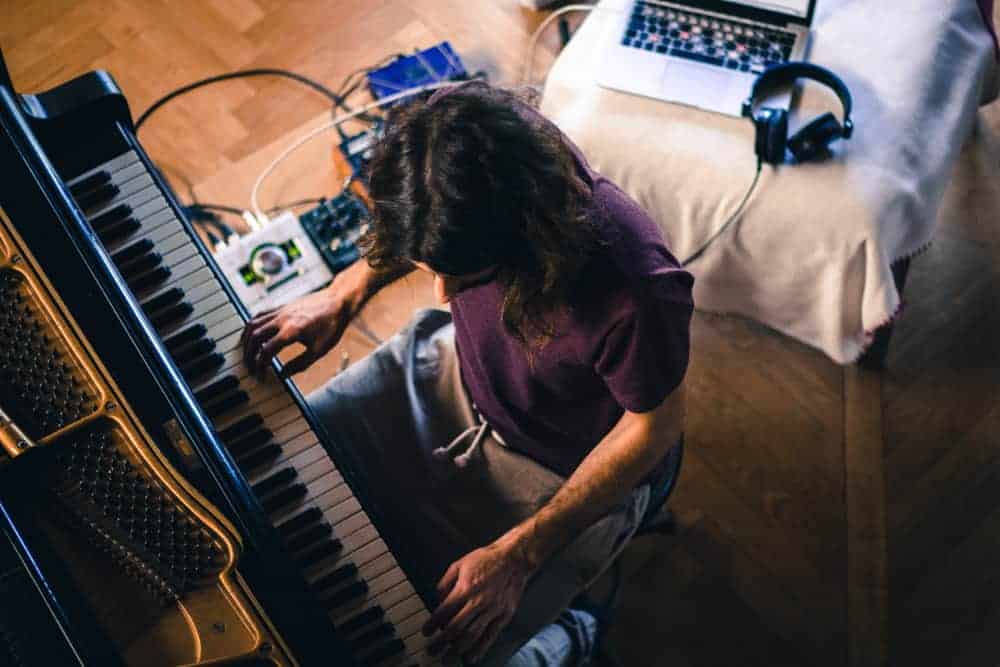 Male musician recording a song on his laptop while playing piano