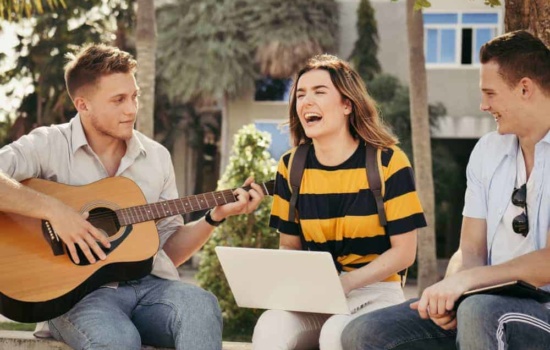 Music business students playing guitar and using computers on campus