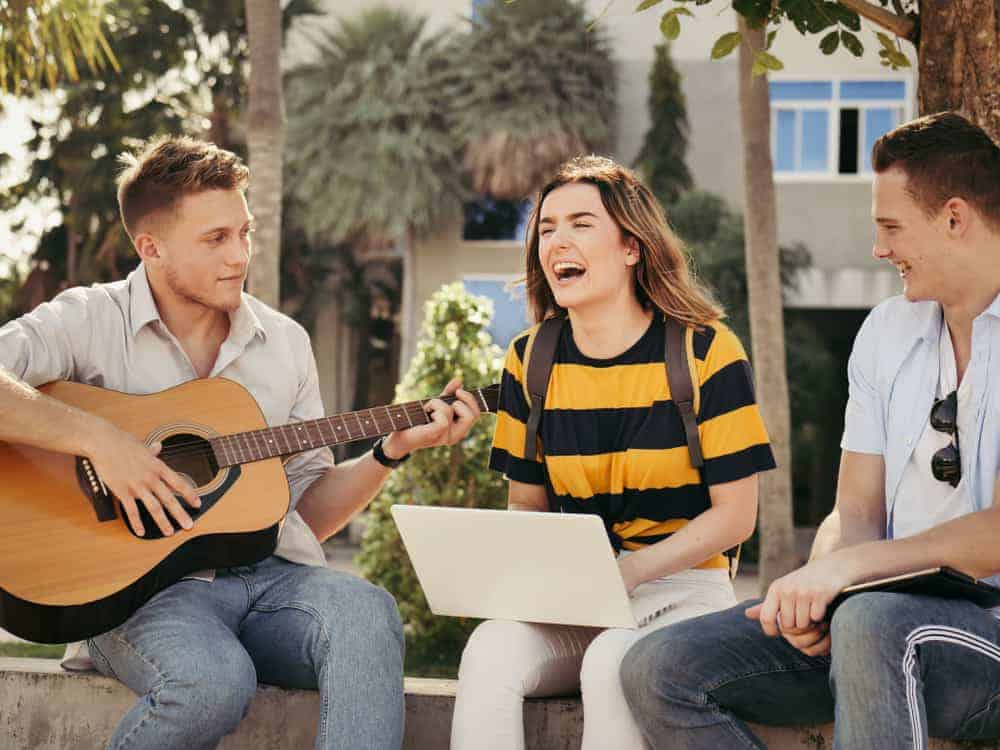 Music business students playing guitar and using computers on campus