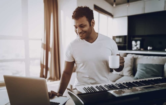 Male musician using laptop to record his keyboard at home