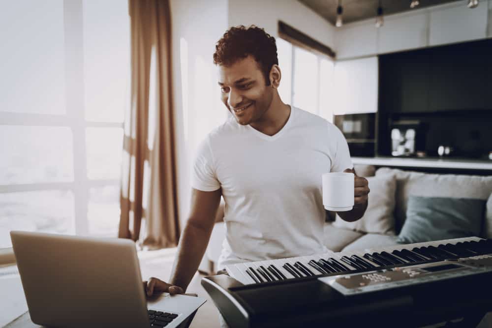 Male musician using laptop to record his keyboard at home