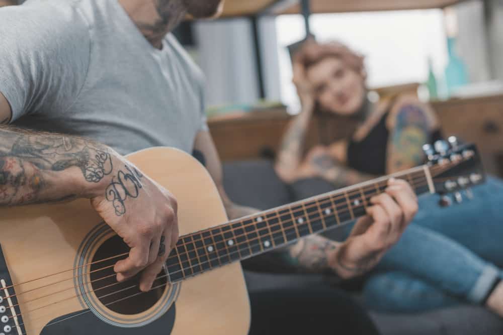 Tattooed male guitarist playing love song while woman listens in background