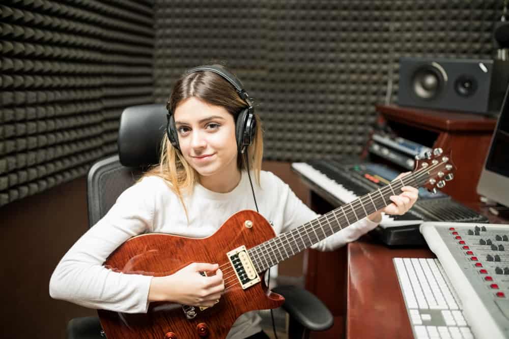 Young female musician playing guitar in recording studio