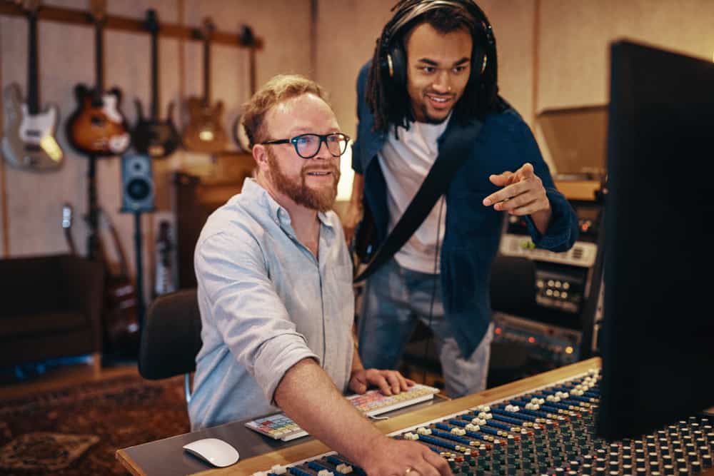 Two male audio producers looking at mixing console and computer in recording studio