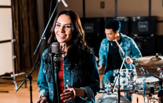 Female singer with condenser mic in studio with male drummer