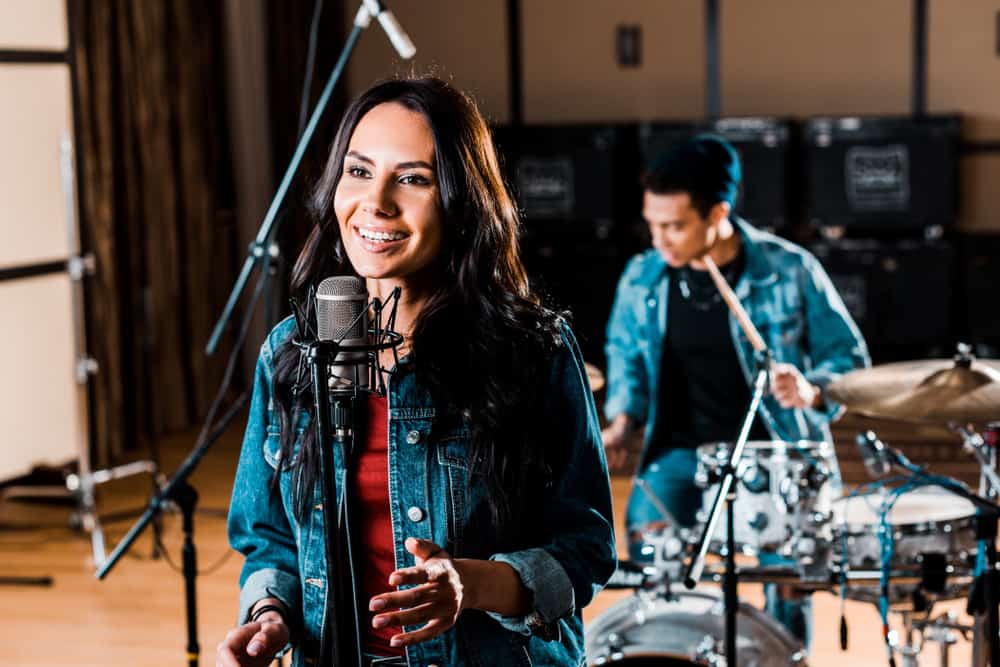 Female singer with condenser mic in studio with male drummer