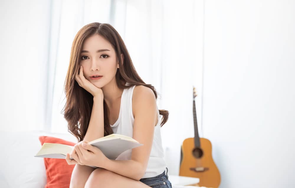 Young woman reading music theory book in bedroom with guitar