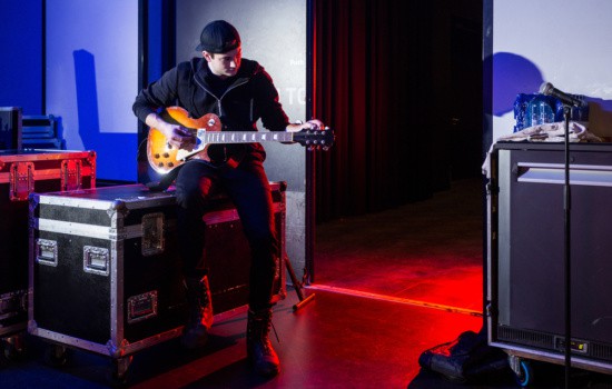 Backstage at concert venue with roadie tuning guitar