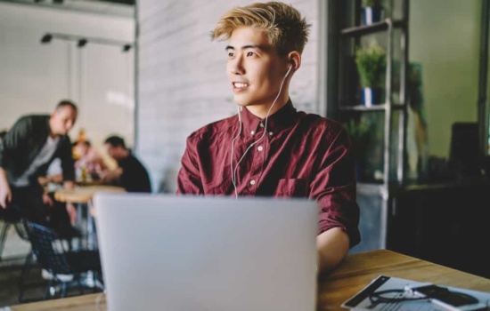 Cool young musician wearing earphones and typing on laptop