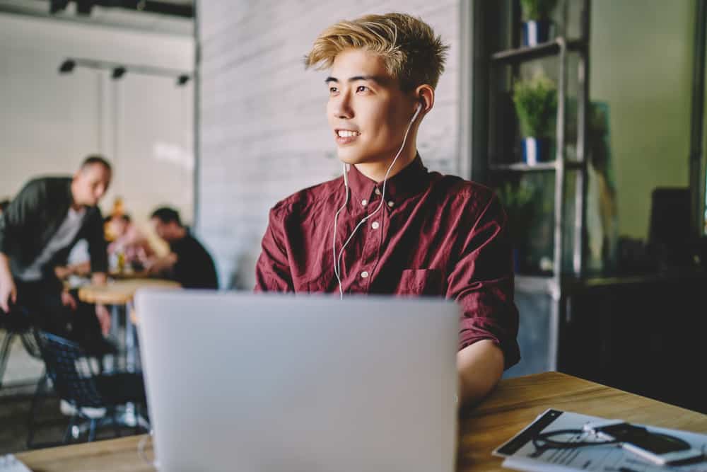 Cool young musician wearing earphones and typing on laptop