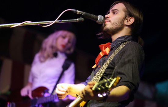 Young male musician playing guitar and singing with female musician in background