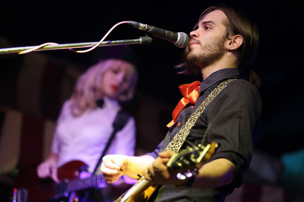 Young male musician playing guitar and singing with female musician in background