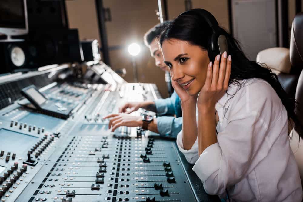 Female audio engineer listening to headphones behind mixing console