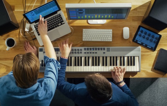 Two musicians producing music on laptop and keyboard