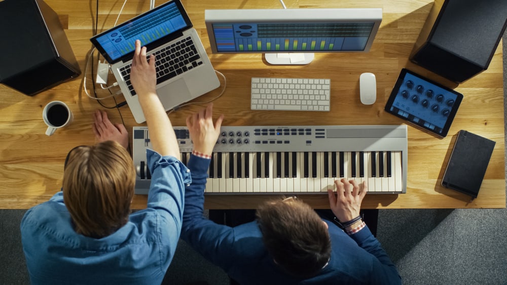 Two musicians producing music on laptop and keyboard