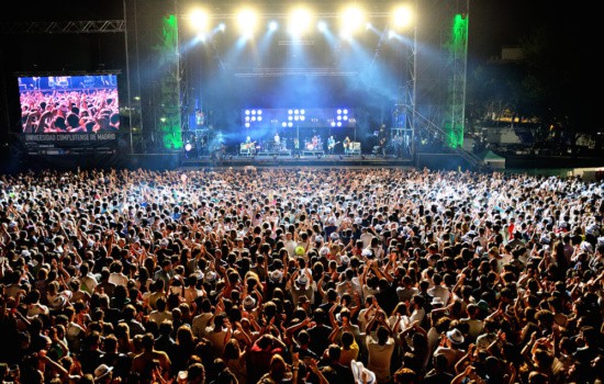 Large concert facility with band onstage and massive crowd of fans