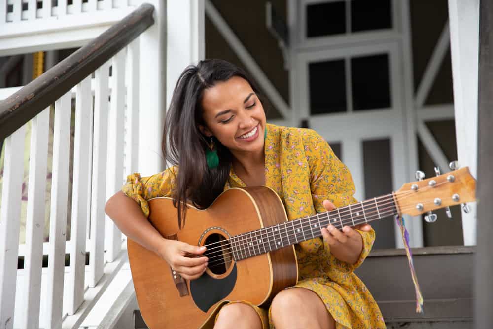 Young female acoustic guitar player on porch