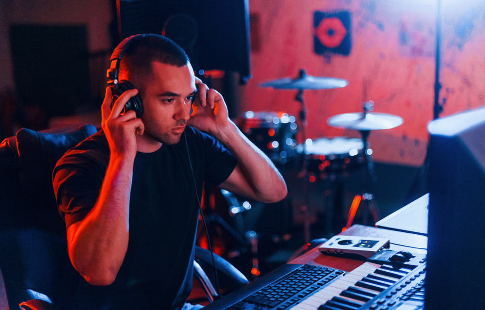 Musician with keyboard listening to his home recordings via headphones