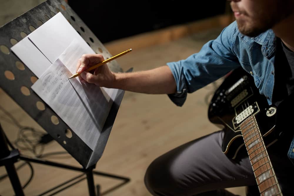 Male guitar player writing on sheet music