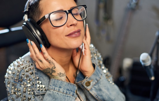 Tattooed female sound engineer listening to music via headphones in recording studio