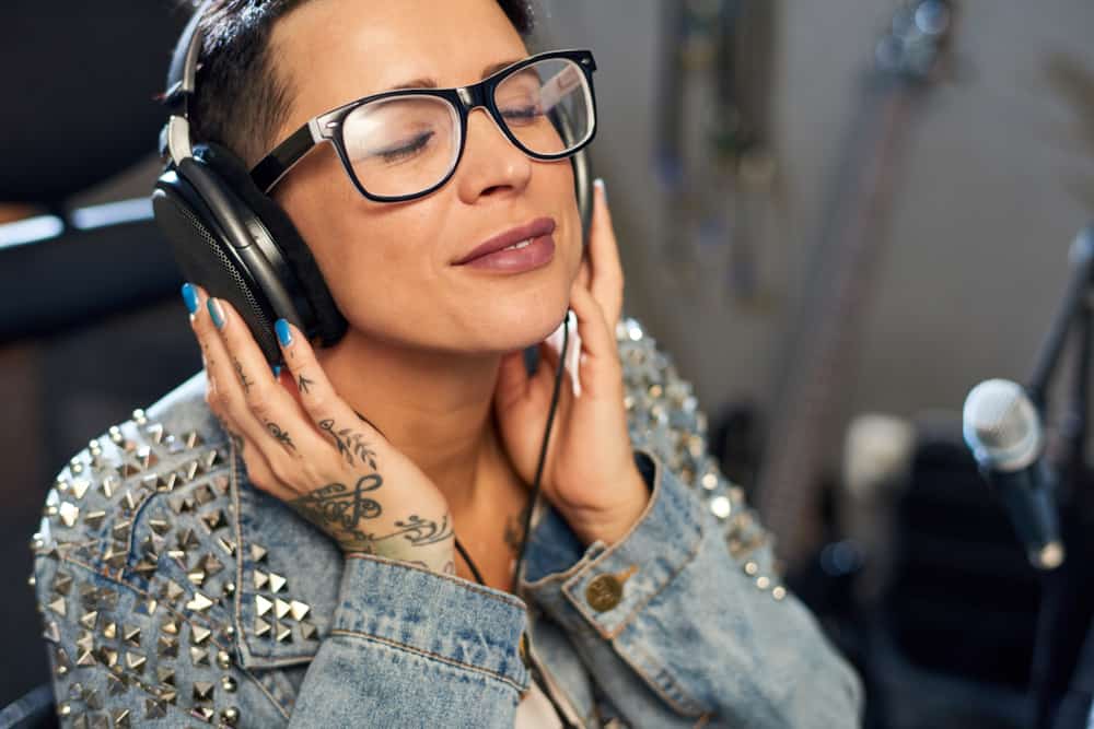 Tattooed female sound engineer listening to music via headphones in recording studio