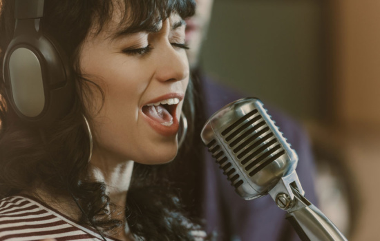 Female singer with microphone and headphones singing in recording studio
