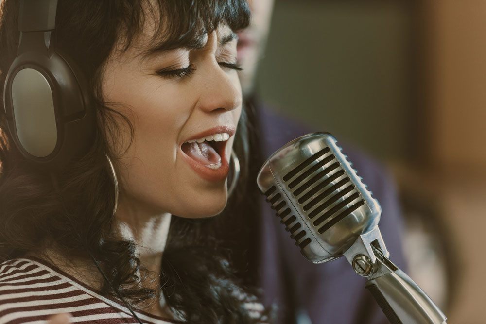 Female singer with microphone and headphones singing in recording studio