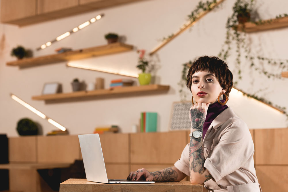 Tattooed staff publicist working on her laptop in large, modern office space
